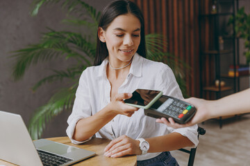Young happy woman wears white shirt hold pay waiter hold mobile cell phone wireless bank payment...