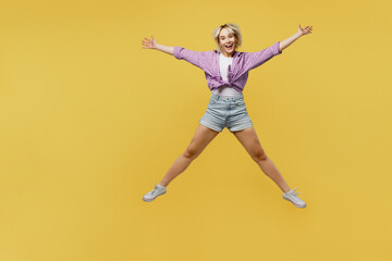 Fototapeta na wymiar Full body young overjoyed excited fun cool blonde woman 20s she wears pink tied shirt white t-shirt jump high with outstretched hands legs isolated on plain yellow background eople lifestyle concept