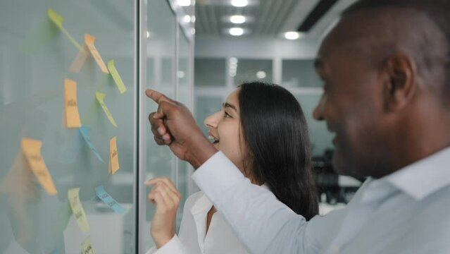 Corporate team business partners colleagues look at paper memo stickers on wall discuss project giving business advice managing tasks structure sticky notes brainstorming teamwork at office meeting