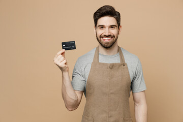 Young man barista barman employee wear brown apron work in coffee shop hold blank screen mobile cell phone point finger camera on you isolated on plain beige background Small business startup concept. - obrazy, fototapety, plakaty
