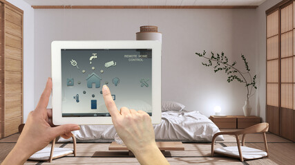 Smart remote home control system on a digital tablet. Device with app icons. Minimalist modern japandi bedroom in the background, architecture interior design