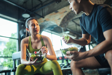 Asian man and woman eating salad for health together. Two Asian people healthy eating salad after exercise at fitness gym. Healthy lifestyle. - obrazy, fototapety, plakaty