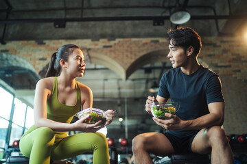 Two Asian people healthy eating salad after exercise at fitness gym. Asian man and woman eating...