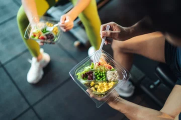 Foto op Plexiglas Fitness Top view Asian man and woman healthy eating salad after exercise at fitness gym. Two athlete eating salad for health together. Selective focus on salad bowl on hand.