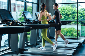 Together Asian man and woman healthy in sportswear cardio exercise jogging on a treadmill in...