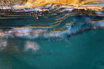 Fototapeta na wymiar Rocky coastline, perpendicular view of the shore, long exposure, blurred waves. Wild coast, illuminated by the pink light of the setting sun, Albania.