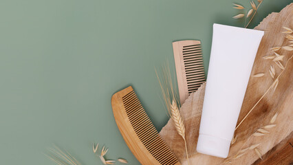 Natural hair cosmetics. Mockup. White bottle with hair beauty product, combs on wooden podium on a green background with rye and wheat ears and copy space. Mock up of natural beauty product for hair