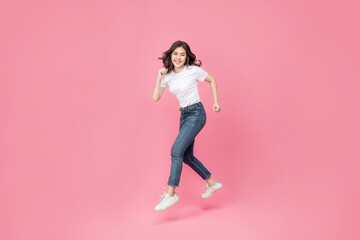 Fototapeta na wymiar Young Asian woman in a white t-shirt cheerful expression on her face as she is very happy over something excited smile and jumping with her arm raised in air on isolated pink background.