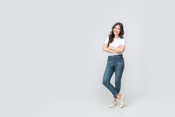 Full length of confident asian woman smiling in a casual outfit in a white t-shirt and jeans, standing with her arm and leg crossed, with a smile on her face on isolated white background. - Powered by Adobe