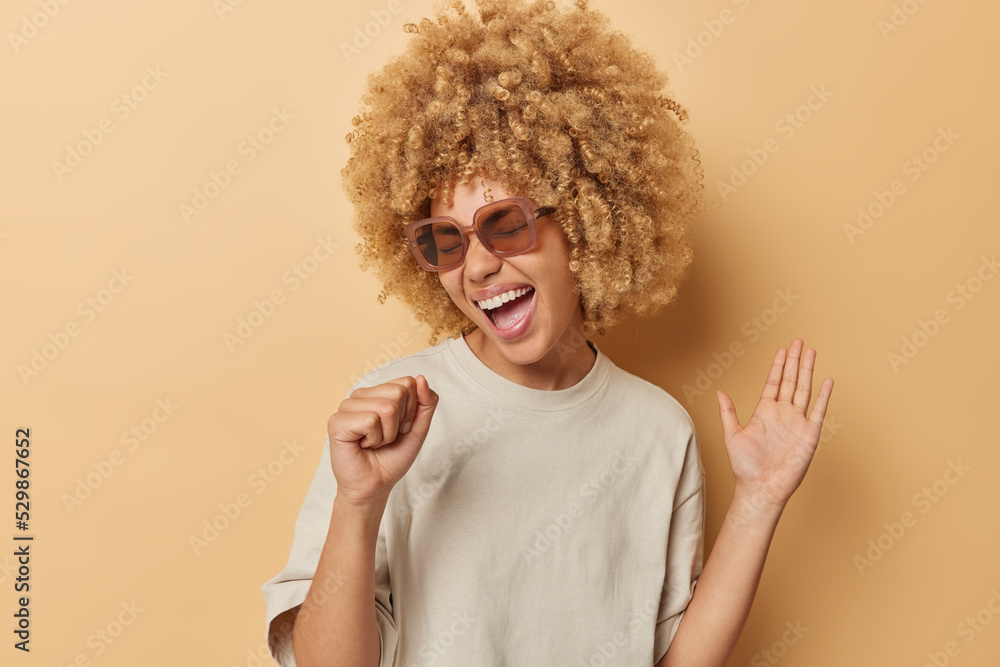 Wall mural positive young woman with cheerful expression keeps hand near mouth like microphone has upbeat mood 