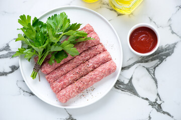 Plate with raw serbian cevapi or cevapcici and fresh parsley on a white marble background, view from above, horizontal shot