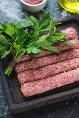 Close-up of raw cevapcici or balkan skinless beef sausages on a black wooden serving tray, vertical shot, selective focus