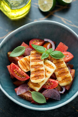 Salad with tomatoes, watermelon and grilled haloumi cheese served in a green bowl, closeup, vertical shot
