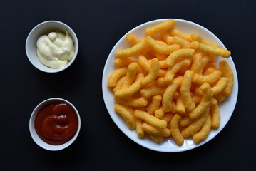 Peppered corn chips with sauce on a black background. Salty snack of corn snacks close-up.