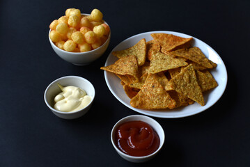 Delicious peppery nachos on a plate with sauces on a black background. Delicious snack with corn nachos close-up. Fast food.