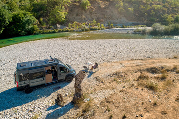 Aerial view of campervan standing on a gravel river beach, camping in wild mountains of Balkans. Adventures and independent van life. Work and travel concept.