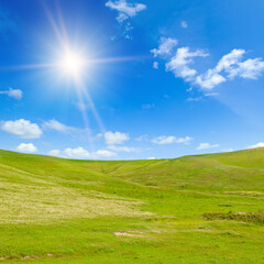 Fototapeta na wymiar Vast grassy meadow with distant hills and sun on sky.