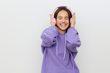 a cheerful, happy woman in a purple tracksuit enjoys music with her eyes closed, holding the headphones with her hands on both sides, smiling pleasantly. Studio Photography