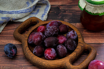 A bowl of fresh blue plums on a wooden background.