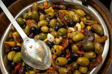 A large mixed vat of olives, peppers, sundried tomatoes and feta cheese in a silver bowl stored in bulk ready to sell smaller measures to consumers in a market looking for fresh home made produce 