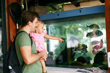 Dad holds a little girl in his arms near an aquarium with fish. High quality photo