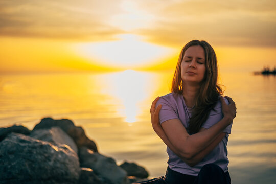 portrait of a woman hugging herself at sunset in summer by the sea
