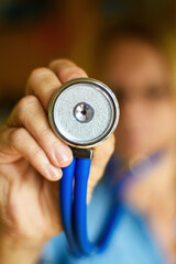  Stethoscope head in sharp focus. Female doctor in soft focus in the background. Unique perspective