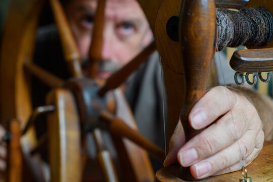 Skilled tradesman works to repair and to intricately fettle the mechanism of an old wooden spinning wheel. Selective focus to accentuate the task of repair and service. Contrasting lighting
