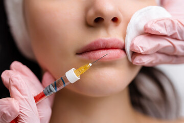 lip shape correction procedure in a cosmetology salon. The specialist makes an injection on the...