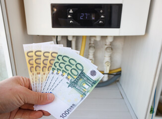 Man is holding banknotes near the boiler. Increase in the price of natural gas. Energy crisis in...