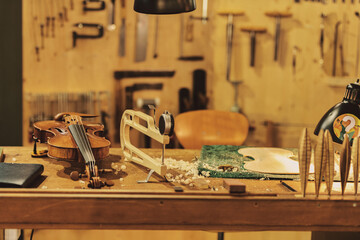 Violin maker workshop. Artisan guitar maker working on the production of a violin.On a wooden table in his workshop are various tools and a violin lies there. Behind it are many tools.