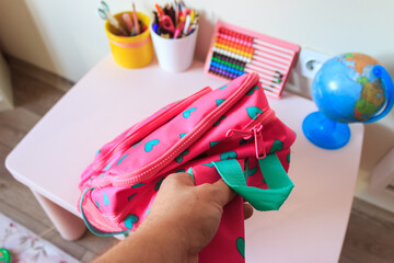 Father is preparing his daughter's pink school bag. Back the school concept.