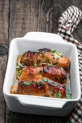 Chicken breasts wrapped in bacon in white dish on wooden table