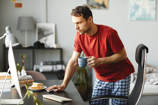 Young man drinking coffee and checking email on his computer at table in the morning at home