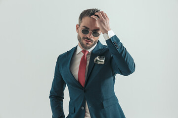 happy unshaved man in suit with retro sunglasses adjusting hair