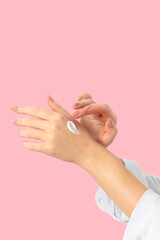 Female hands on a pink background smear cream, long beige nails, manicure and gel polish. Woman taking care of her skin and body