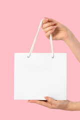 Mockup female hands hold a white paper stylish package, bag on a pink isolated background. Empty template for your design and logo