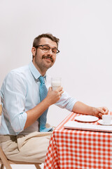 Portrait of smiling man in official clothes sitting at the table and heaving breakfast. Looks calm and delightful