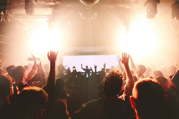 DJ performing at nightclub with crowd of people with their hands up
