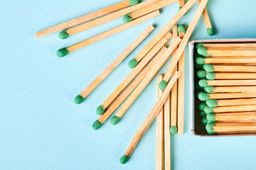 A lot of matches with green heads in a matchbox and near the box on a blue background with copy space