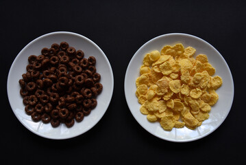 Breakfast of chocolate and honey cornflakes on white plates on a black background. Delicious breakfast of cornflakes close-up.