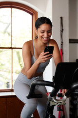 Fototapeta na wymiar Young biracial woman using mobile phone while on exercise bike at the gym