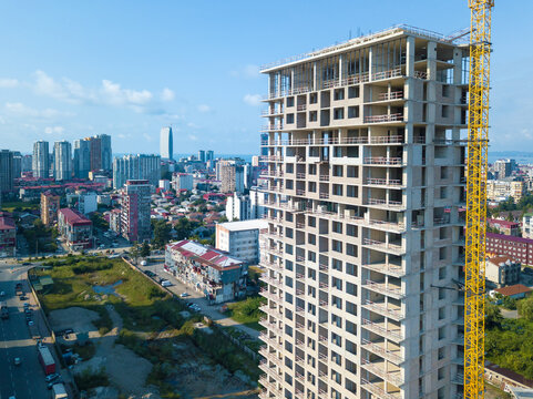 Drone view of a large construction site with a tower crane, an almost completed multi-storey house in the city on a sunny day. Multi-storey residential building is being built using a crane.