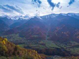 Obraz premium Beautiful view from a drone of a village at the foot of the mountains on an autumn day. Beautiful autumn landscape with autumn trees, snow-capped mountains