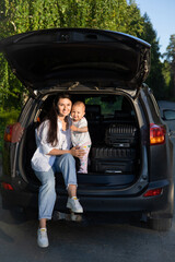 Car journey. Travel with a child by car. Mother and daughter sit in a car with an open trunk