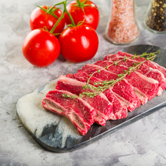 Cooking homemade meat steaks. On a cutting board, appetizing pieces of raw meat with a sprig of rosemary, red tomatoes, spices in glass jars on a light background. Banner.
