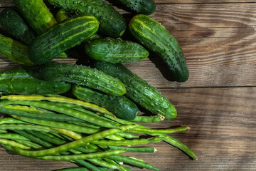 Green farm vegetables cowpea beans and cucumbers on a wooden background.