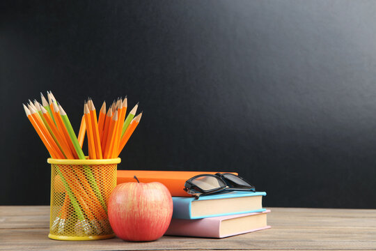 Apple, pencils in basket, eyeglasses and books on black chalkboard background with copy space. Concept teachers day