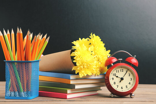 Bouquet of yellow chrysanthemums, colorful notepads, alarm clock and pencils in basket on black background. Concept teachers day