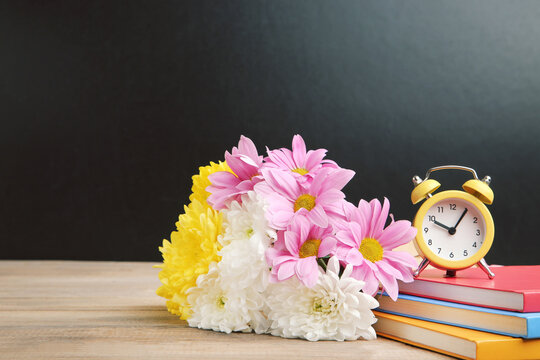 Bouquet of colorful chrysanthemums, notepads and yellow alarm clock on black background with copy space. Concept teachers day